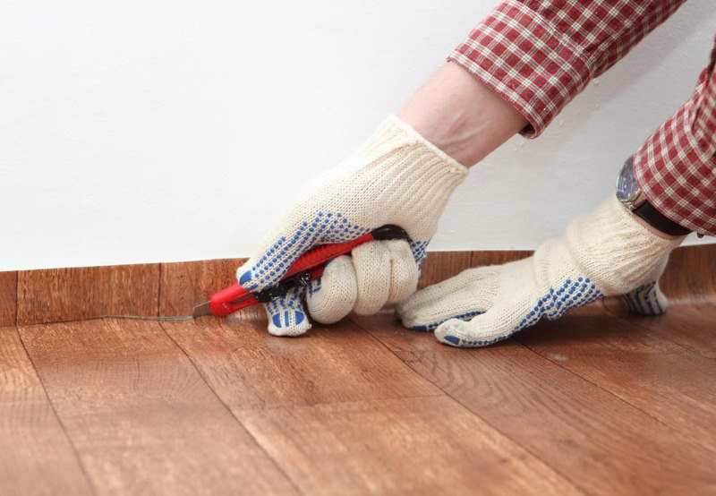 Rifilatura fai-da-te dei bordi del linoleum lungo il muro con un coltello da costruzione