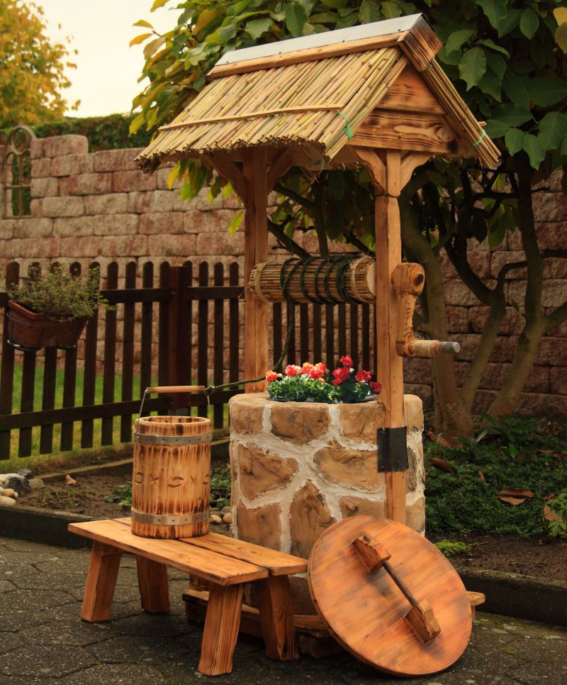 Piccola forma architettonica per il giardino sotto forma di un pozzo decorativo in pietra e legno