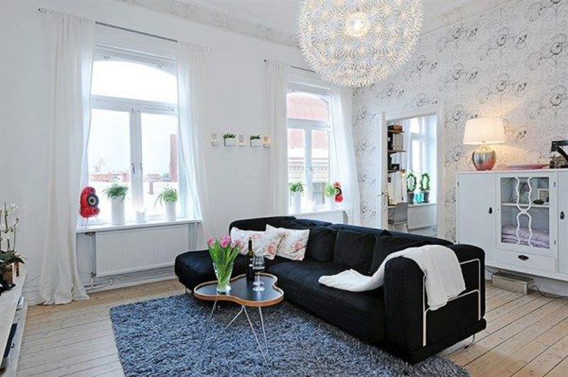 Black sofa in the middle of a spacious living room with two windows