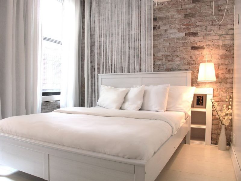 White bed in a bedroom with a brick wall