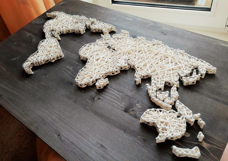 World map of nails and threads on a wooden surface