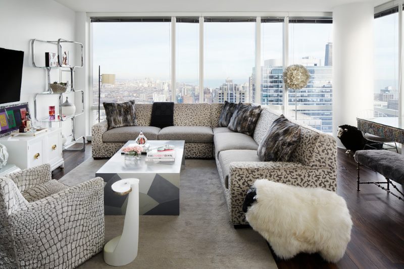 Canapé avec coussins gris et beiges dans le salon avec de grandes fenêtres